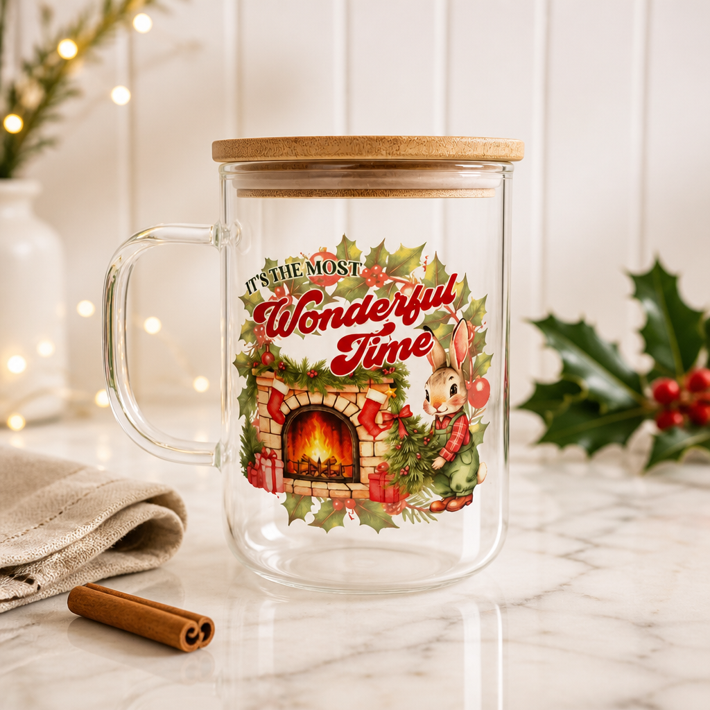 A clear glass mug with a bamboo lid, decorated with a festive Christmas illustration featuring a bunny, fireplace, holly, and the words 'It's the Most Wonderful Time.' This is the perfect compliment to your cozy evenings in!